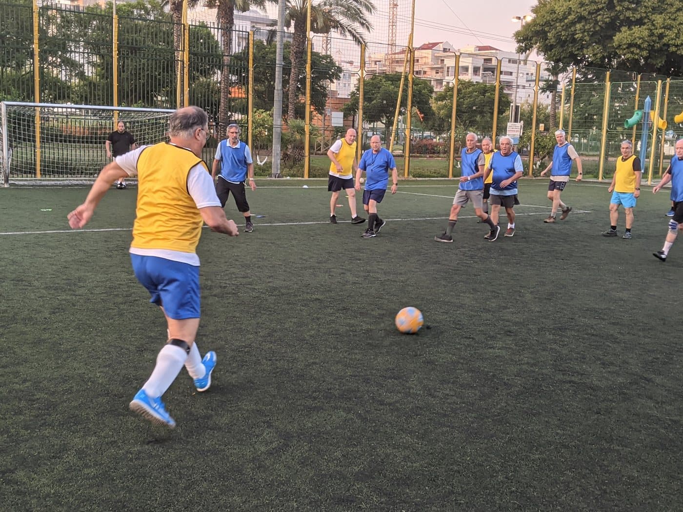 Older adults playing a casual soccer match in yellow and blue bibs